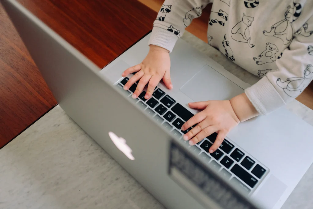 Tiny toddler hands on a laptop keyboard, symbolizing a working mom juggling business tasks and parenting at home in 2025.