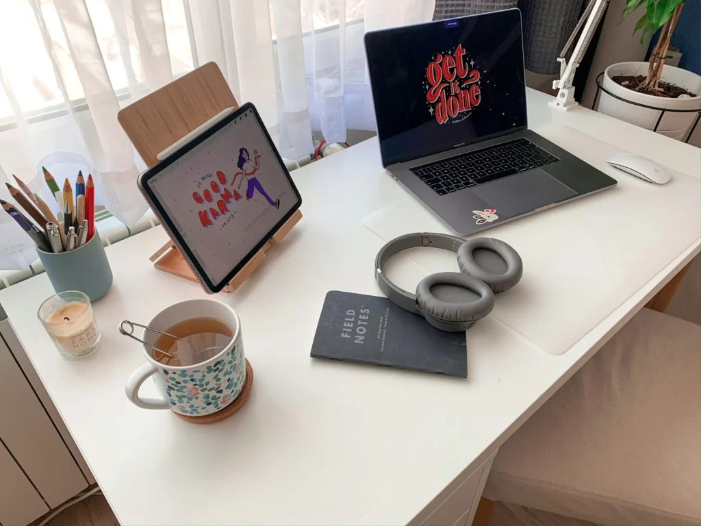 The Honest Truth About Balancing Art and Business 1 Minimalist creative workspace setup for balancing creativity and business — with a laptop, digital sketch on tablet, tea, and planner on a white desk