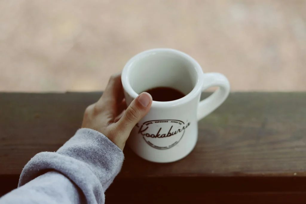 Simple Pleasures: Why I Fell in Love with Country Living 1 Hand holding white coffee mug on a wooden porch railing, peaceful country morning — simple pleasures moment.
