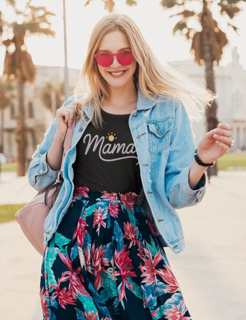 Smiling woman in a black Mama t-shirt with sun icon, wearing a floral skirt and pink sunglasses – promoting Happily Styled summer collection